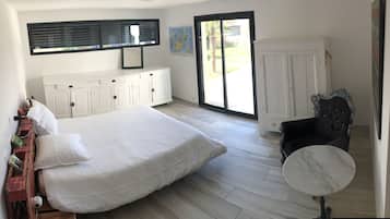 A bedroom with a bed, a white dresser, a black chair, and a small round table.
