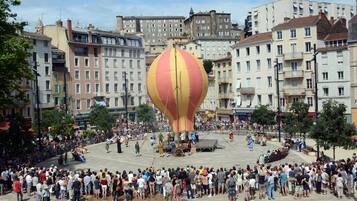 Una plaza pública con una gran multitud reunida alrededor de un globo aerostático.