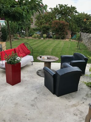 Un espacio al aire libre con una maceta roja, una mesa redonda y sillas negras.