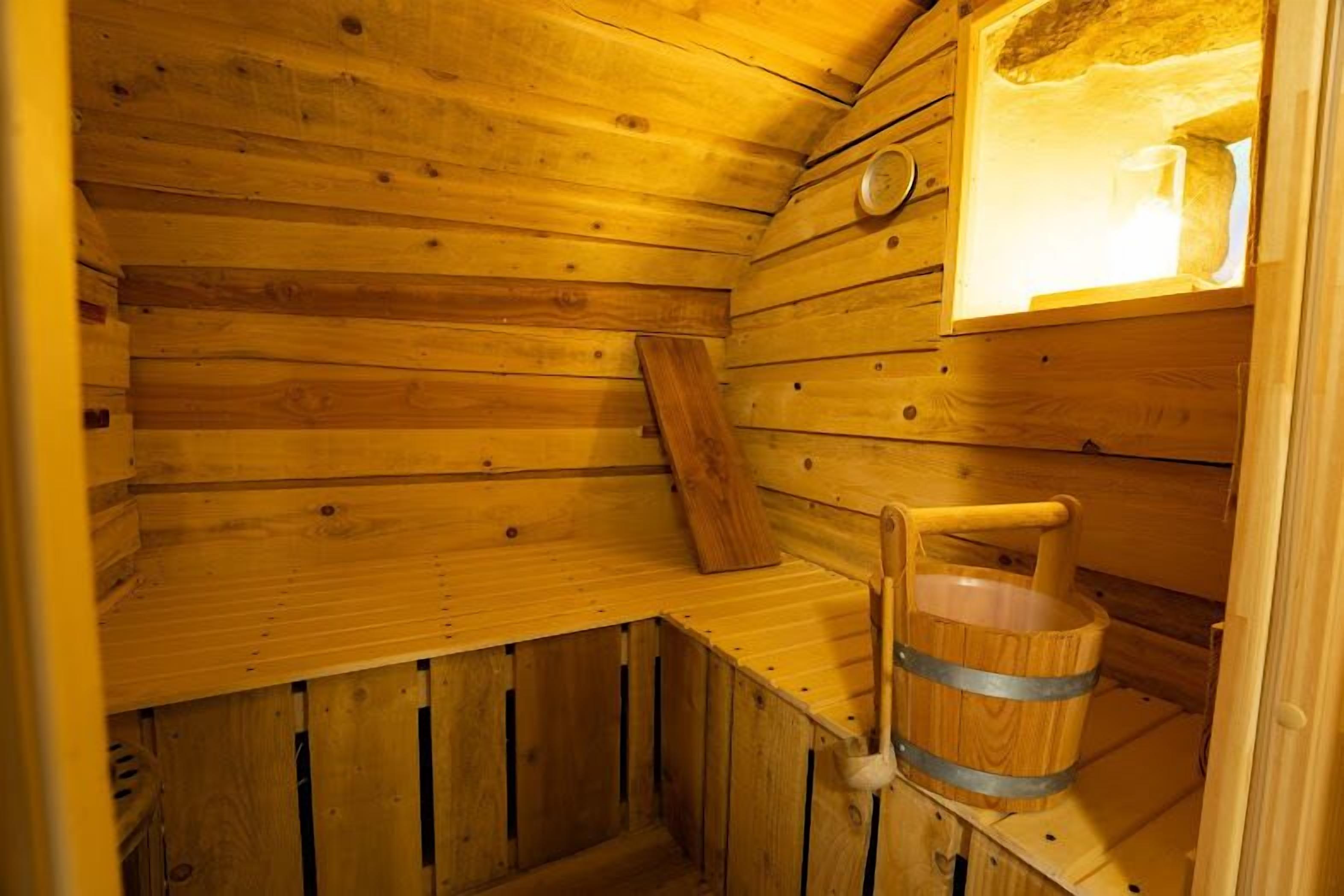 A wooden sauna room with a bench, a bucket, and a window.