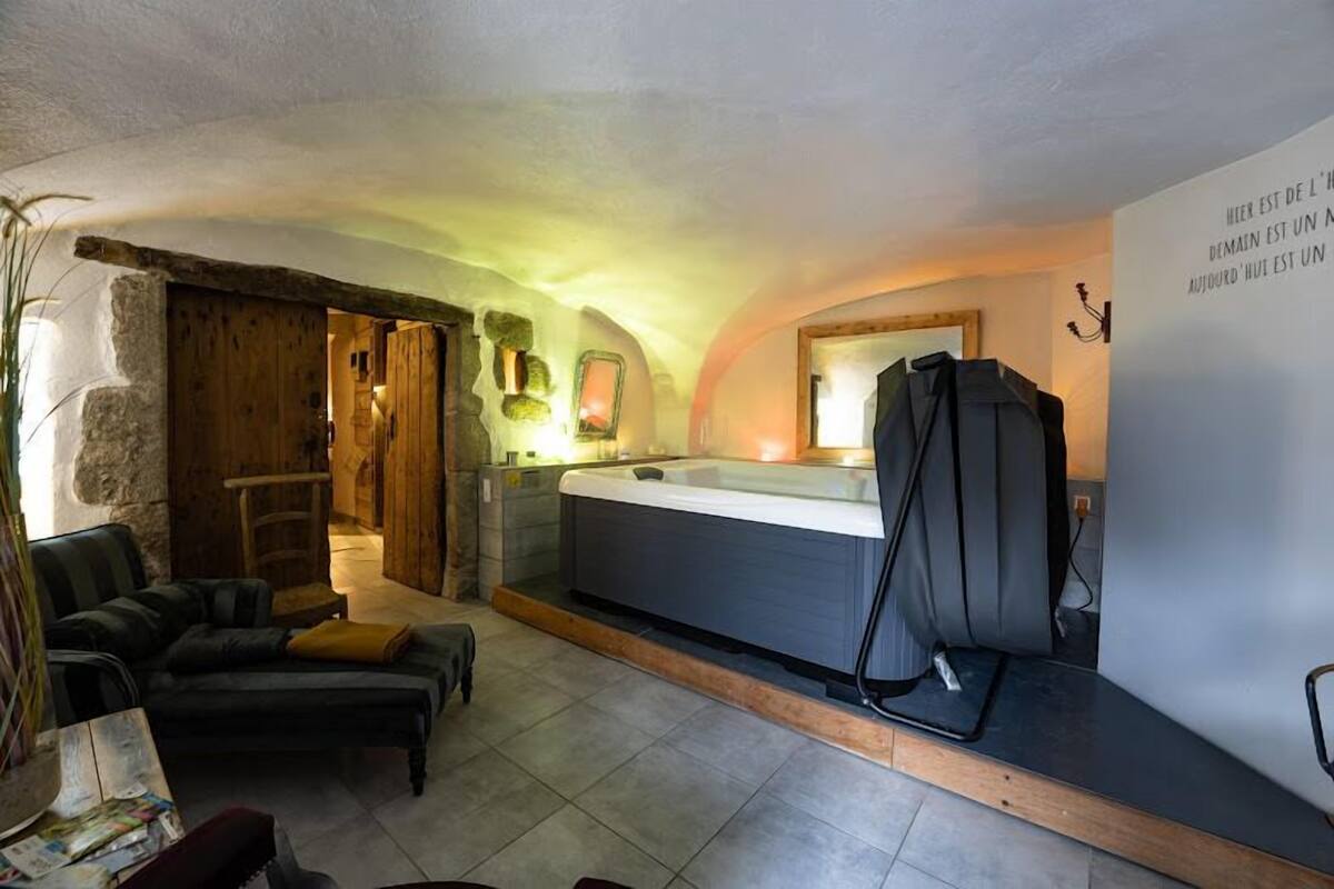 Un saló confortable amb un sofà, una taula de centre i una llar de foc. Es pot veure una banyera d'hidromassatge al fons i una porta de fusta que condueix a una altra habitació.