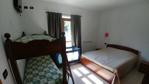 A bedroom with two beds, a window with curtains, a radiator, and a small desk. - Agriturismo Bastià (Corio)