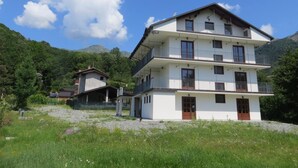 A multi-story building with balconies, set in a mountainous area with greenery and clear skies. - Agriturismo Bastià (Corio)