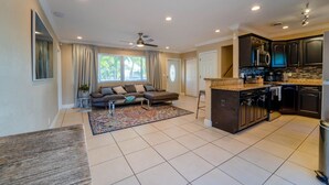 A spacious living area with a sofa, a coffee table, and a rug. There is a kitchen with dark cabinets and a countertop. - "Palm Estate" - Spacious 3 bed, 3 bath, 2 story single family home with pool (Hallandale Beach)