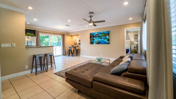 A spacious living room with a brown leather sofa, a glass coffee table, and a dining area with a kitchen in the background. - "Palm Estate" - Spacious 3 bed, 3 bath, 2 story single family home with pool (Hallandale Beach)
