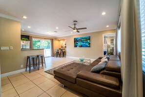 A spacious living room with a brown leather sofa, a glass coffee table, and a dining area with a kitchen in the background. - "Palm Estate" - Spacious 3 bed, 3 bath, 2 story single family home with pool (Hallandale Beach)