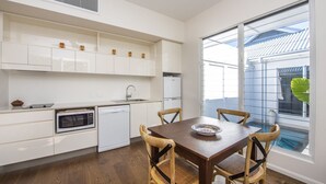 A modern kitchen with white cabinetry, a built-in oven, and a dining area with a wooden table and chairs. - Reflections Topaz Villa 3 (Picnic Bay)