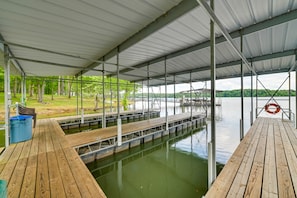 A covered dock area with a wooden walkway leading to a body of water, surrounded by trees and a distant view of hills. - Cozy Dover Home w/ Boat Dock, Fire Pit & Deck! (Dover)