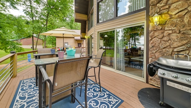 An outdoor deck with a table and chairs, a grill, and a stone wall.