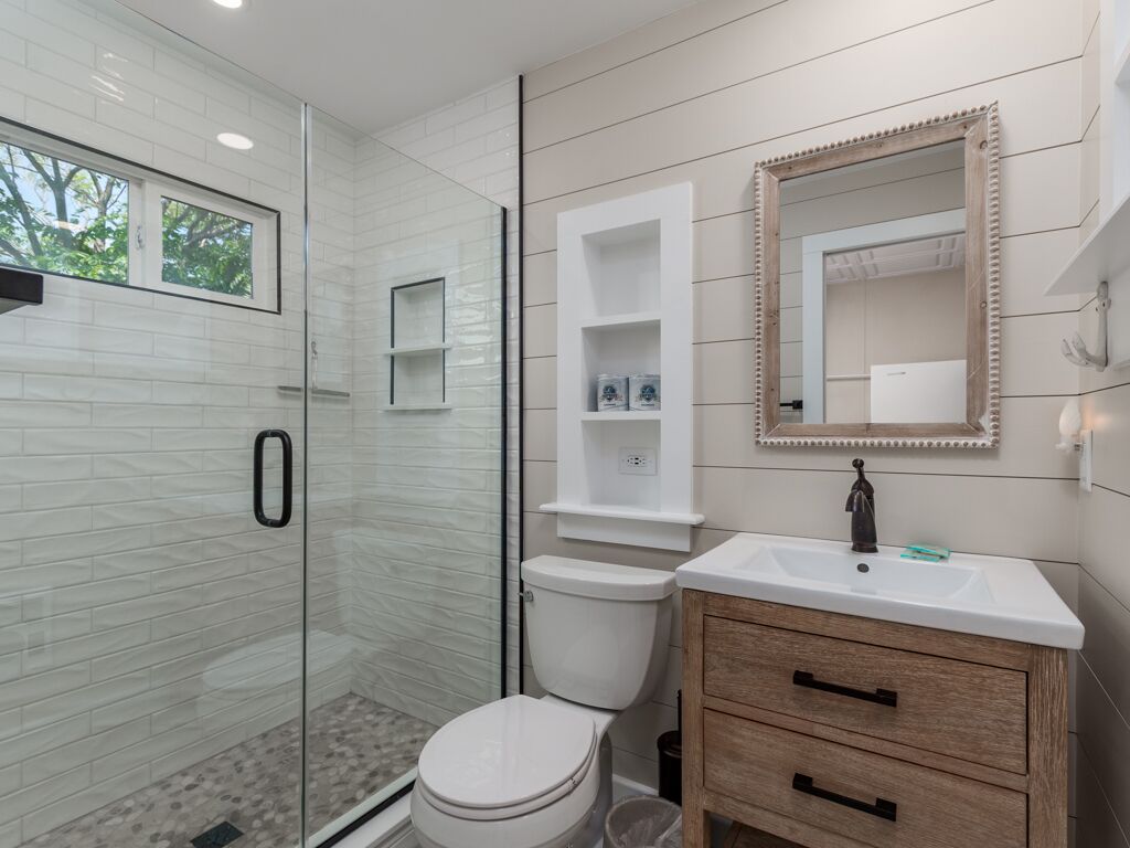 A modern bathroom with a glass shower enclosure, a toilet, a vanity with a mirror, and built-in shelves.