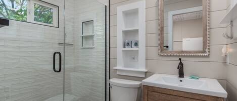 A modern bathroom with a glass shower enclosure, a toilet, a vanity with a mirror, and built-in shelves.
