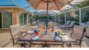 An outdoor patio with a table set for four, surrounded by chairs, and a large umbrella providing shade.