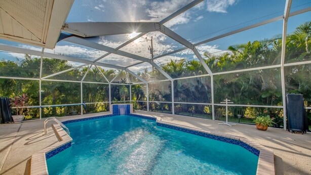 A covered swimming pool with a clear view of the surrounding greenery and a blue-tiled edge.