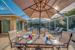 Eine Terrasse im Freien mit einem Tisch für vier Personen, umgeben von Stühlen, und einem großen Sonnenschirm, der Schatten spendet.