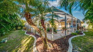 A modern house with a glass conservatory, surrounded by a well-maintained garden with palm trees and a stone pathway.