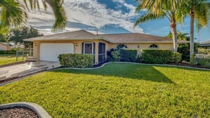 A single-story house with a garage, surrounded by well-maintained lawns and palm trees.