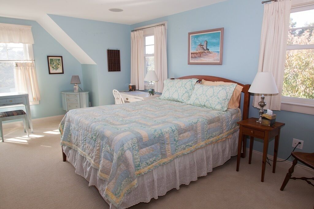 A bedroom with a bed, a desk, a chair, and a window with curtains.