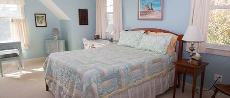 A bedroom with a bed, a desk, a chair, and a window with curtains.