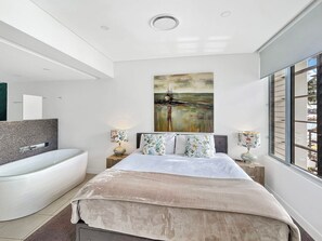 Een moderne slaapkamer met een groot bed, een badkuip en een schilderij aan de muur.