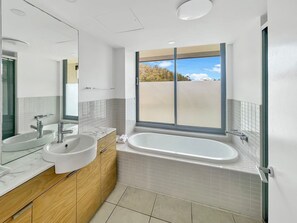 Een moderne badkamer met een groot raam, een bad en twee wasbakken.