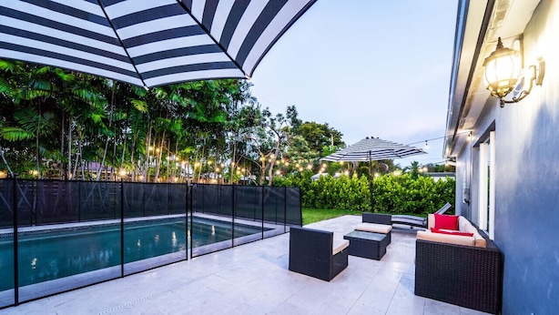 A poolside area with a glass enclosure, outdoor furniture, and string lights. - Grey Manor – Spacious 3BR/2BA Hallandale Home, Heated Pool & Smart Amenities (Hallandale Beach)