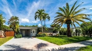 A single-story house with a front yard, palm trees, and a clear sky. - Grey Manor – Spacious 3BR/2BA Hallandale Home, Heated Pool & Smart Amenities (Hallandale Beach)