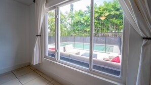 A room with a large window overlooking a swimming pool and lush greenery. - Grey Manor – Spacious 3BR/2BA Hallandale Home, Heated Pool & Smart Amenities (Hallandale Beach)
