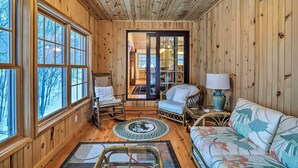 A cozy wooden interior with large windows, a wicker sofa, a chair, and a small table with a lamp. - 2 Mi to Schuss Mtn! Northern Retreat w/ Game Room (Bellaire)