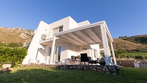 A modern white house with a covered patio, stone foundation, and a view of a hilly landscape. - Villa Cristina - Relax - Pool and Sea View (Castellammare del Golfo)