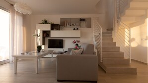 A modern living room with a sofa, a coffee table, a flat-screen TV, and a staircase. - Villa Cristina - Relax - Pool and Sea View (Castellammare del Golfo)