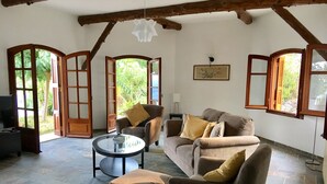 Een gezellige woonkamer met een stenen vloer, een bank met kussens, een ronde salontafel en een televisie.