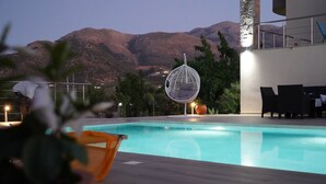 A pool area with a hanging chair, a table, and chairs, surrounded by potted plants and a mountainous backdrop. - Villa Callista with Private Pool and Hot Tub (Sissi)