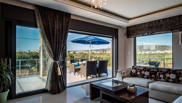 A spacious living room with a large sliding glass door leading to a balcony, a sofa with patterned cushions, a coffee table, and a chandelier. - Villa Callista with Private Pool and Hot Tub (Sissi)
