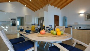 Een moderne keuken met witte kasten, een houten plafond en een eethoek met blauwe stoelen en een tafel voor vier personen.