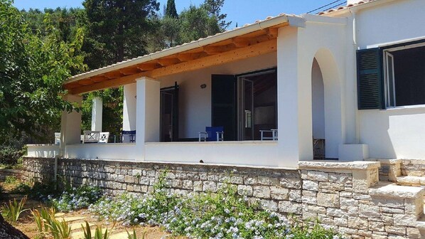 Une maison moderne dotée d’un porche abrité, de fondations en pierre et d’un jardin agrémenté de fleurs blanches.