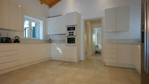 Een moderne keuken met witte kasten, een inbouwoven en een magnetron. Er is een raam dat natuurlijk licht binnenlaat en een deur naar een andere kamer.