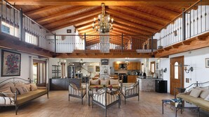 A spacious loft-style living area with high ceilings, a central seating arrangement, and a kitchen in the background. - Prestige Villas  |  NISSAKI  |  5* Stone Olive Press, Large Pool with Sea Views (Corfu)