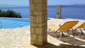 A stone pillar, a pool, and two sun loungers with a view of the sea. - Prestige Villas  |  NISSAKI  |  5* Stone Olive Press, Large Pool with Sea Views (Corfu)