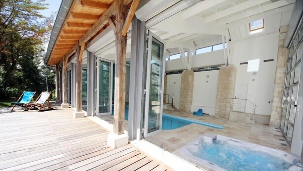 Un área de piscina exterior moderna con un solárium de madera, puertas de vidrio y un muro de piedra.