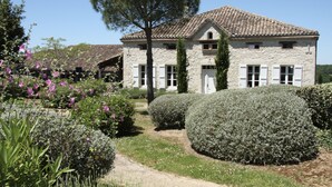Un edificio de piedra con techo de tejas, rodeado de jardines y setos bien cuidados.