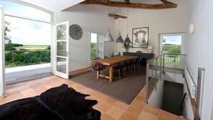 Un comedor amplio con una mesa y sillas de madera, un ventanal con vistas a la vegetación y una viga rústica en el techo.
