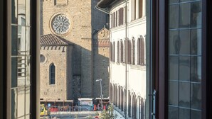 A view through a window of a historic building with a clock tower, a church, and a street with a yellow vehicle. - Zip b&b in Florence (Florence)