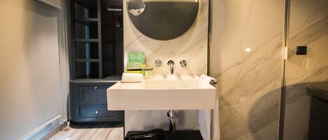 Un baño moderno con un lavamanos blanco, un espejo redondo y un perchero para toallas.