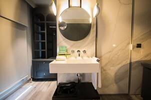 Un baño moderno con un lavamanos blanco, un espejo redondo y un perchero para toallas.