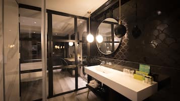Un baño moderno con entrada de puerta de cristal, un lavamanos blanco y un espejo con marco circular.