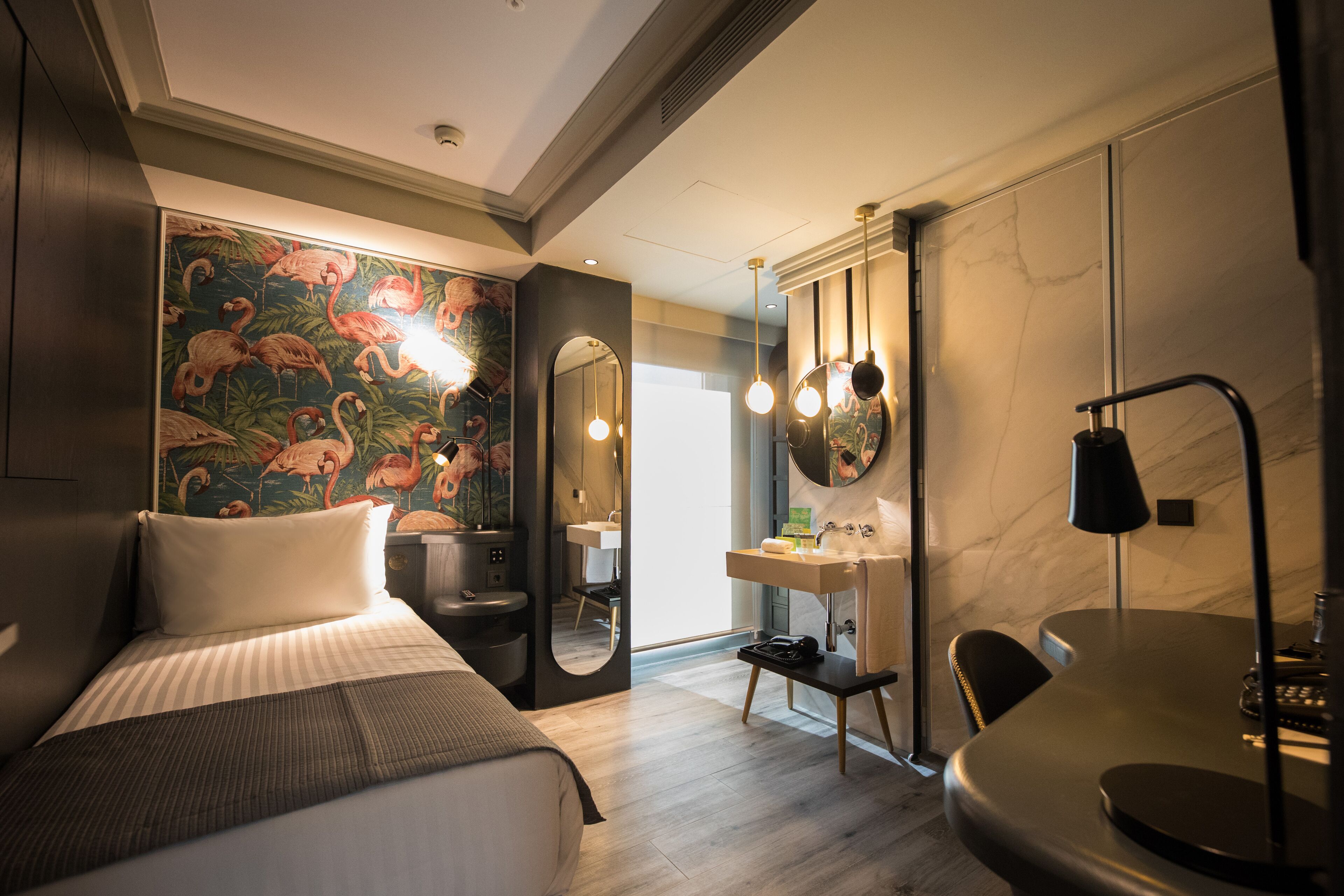 Una habitación de hotel moderna con una cama, un escritorio, un espejo, un baño con lavamanos y un espejo grande.