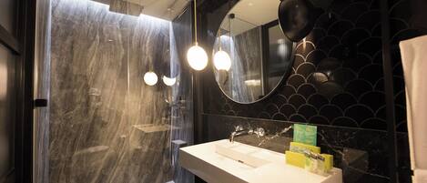 Un baño moderno con ducha envuelta en vidrio, un lavabo blanco y un espejo grande con un detalle decorativo en la pared.