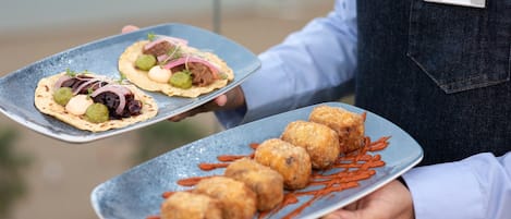 Una persona sosteniendo dos platos de comida, uno con tacos y otro con buñuelos, en un entorno al aire libre.