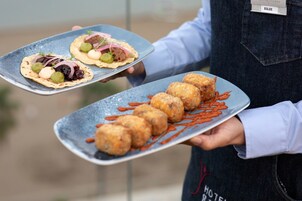 Una persona sosteniendo dos platos de comida, uno con tacos y otro con buñuelos, en un entorno al aire libre.