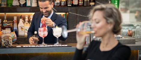 A bar with a bartender preparing drinks and a customer holding a cocktail.